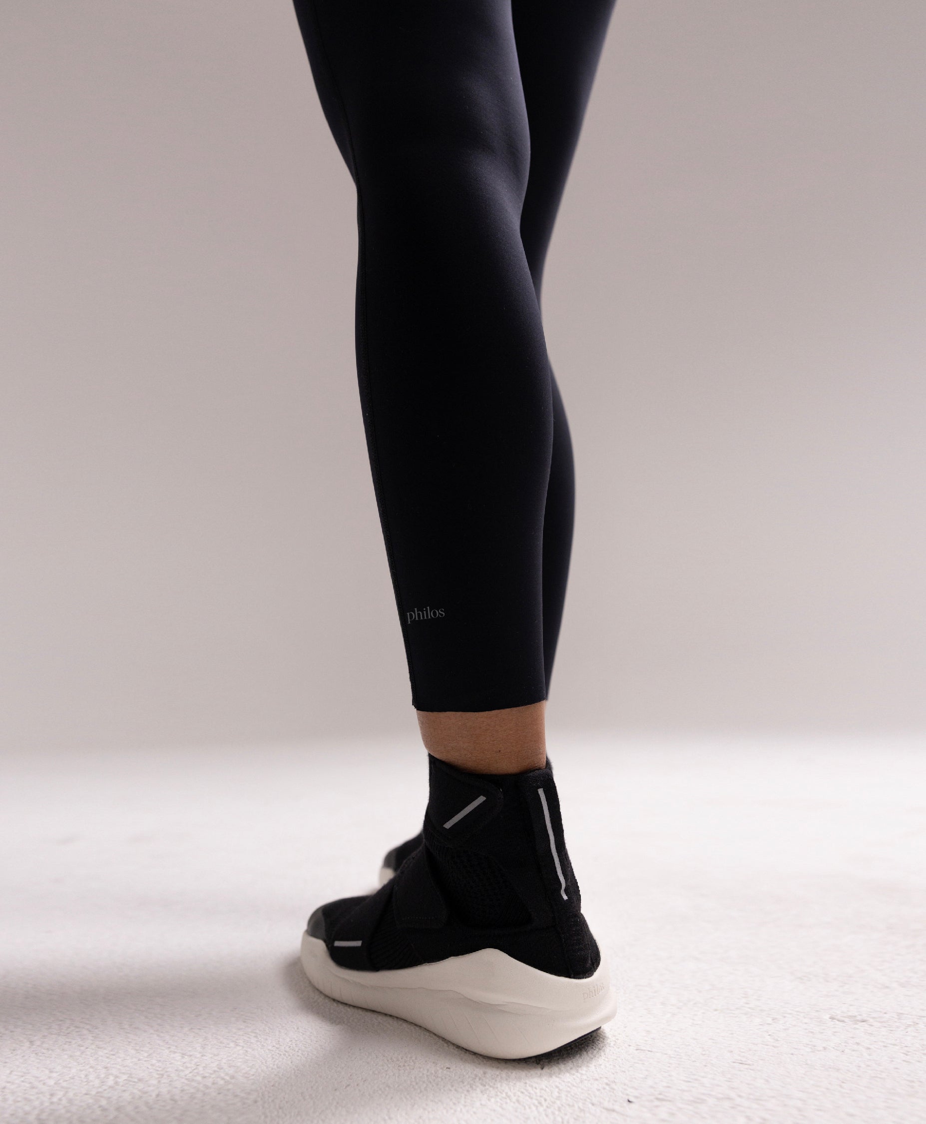 Close up of the Philos Running Tights for women in black, showcasing the laser-cut hems, and reflective logo for functional performance.