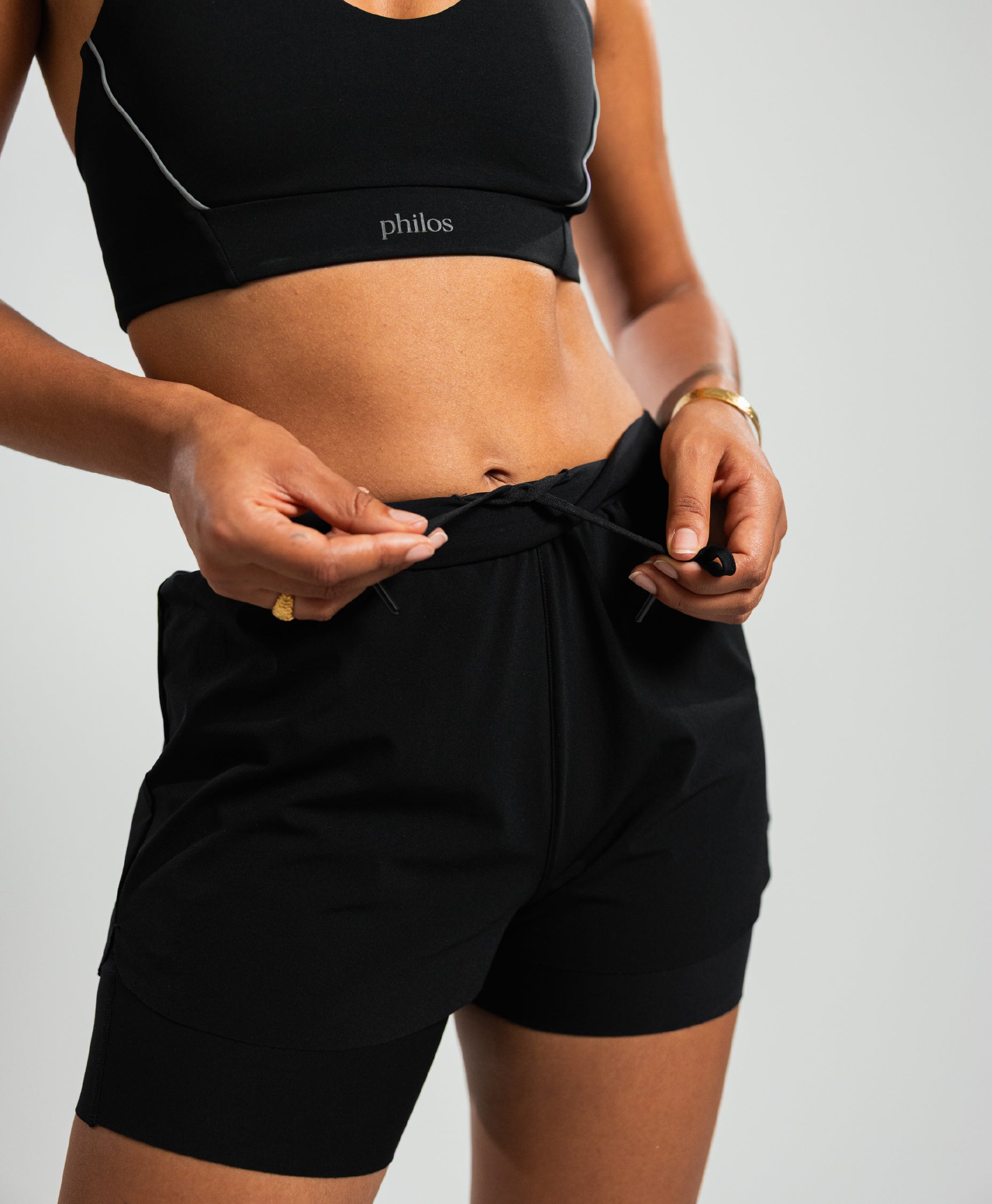 Front view of the Philos 2 in 1 running shorts for women, in black. They feature a high-waisted design, hidden drawstring and a concealed phone pocket.
