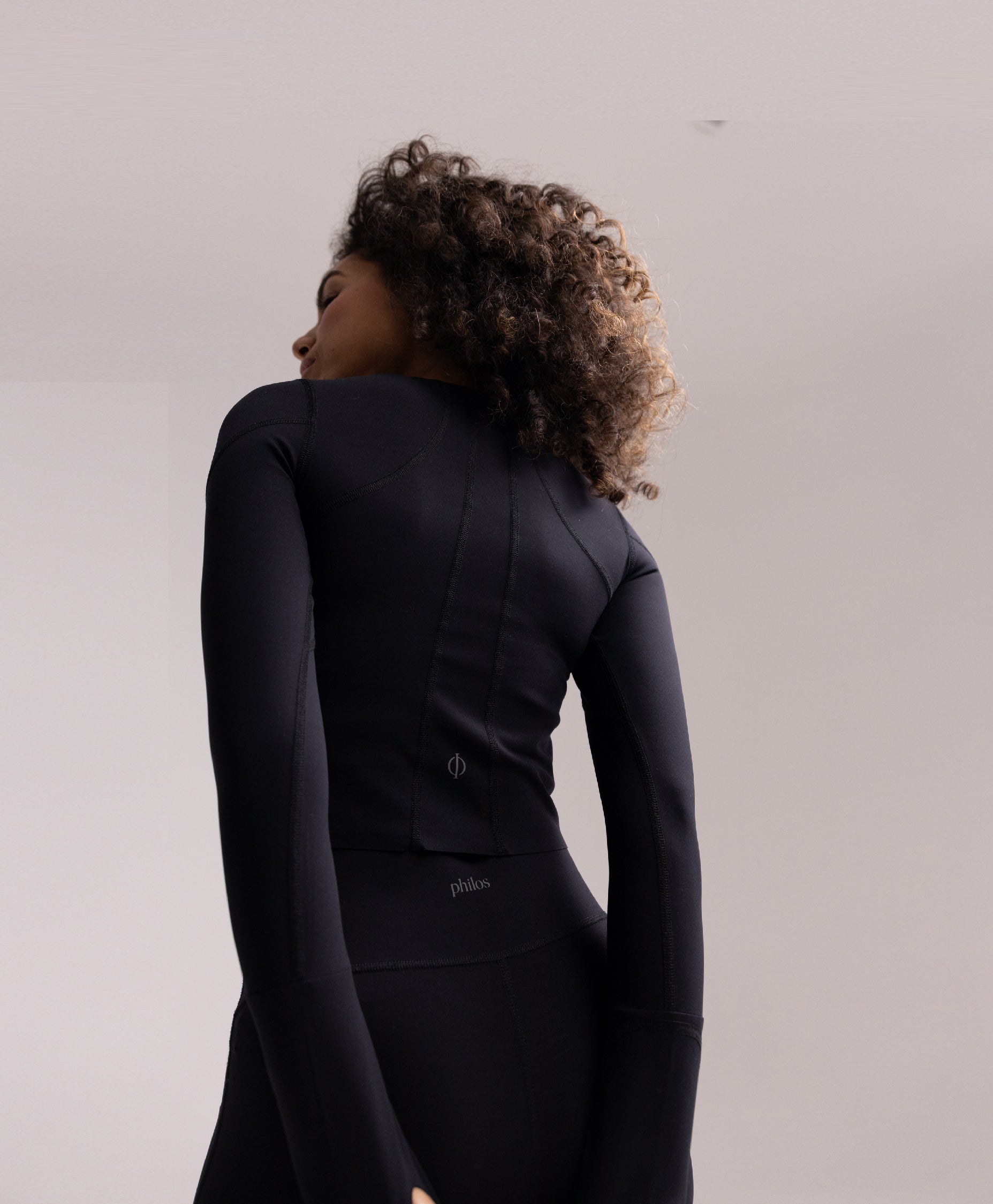 Back view of the Philos Armor Running Long Sleeve, highlighting the cropped fit, and anatomically inspired seams that follow the natural lines of the spine and shoulders.